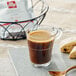 A glass cup of illy Classico Lungo coffee on a saucer next to a pastry.