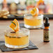 A glass of King Floyd's Cardamom Bitters added to a glass of orange drink with an orange slice.