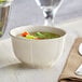 An Acopa Warm Gray porcelain bouillon cup filled with soup and vegetables on a table.