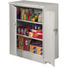A light gray Tennsco deluxe storage cabinet with solid doors filled with boxes and cans.