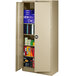 A tan metal Tennsco storage cabinet with solid doors and shelves full of books.