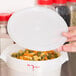 A person's hand holding a Cambro white plastic lid over a white container of pasta.