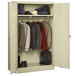 A Tennsco putty metal wardrobe cabinet with solid doors filled with clothes and shoes.