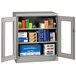 A light grey metal Tennsco storage cabinet with C-Thru doors holding many boxes.