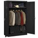 A black metal Tennsco wardrobe cabinet with solid doors and clothes on hangers inside.