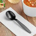 A black Visions plastic soup spoon on a napkin next to a bowl of soup.
