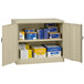 A sand Tennsco storage cabinet with solid doors open to reveal boxes on shelves.