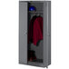 A dark gray Tennsco deluxe wardrobe cabinet with solid doors holding a red jacket and helmet.