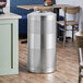 A Lancaster Table & Seating stainless steel round waste receptacle with feet.