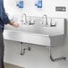 A person washing hands with soap under 3 wall mounted faucets at a Regency Multi-Station Hand Sink.
