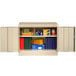 A sand Tennsco standard storage cabinet with solid doors storing books and folders.