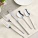 Acopa Penn Square stainless steel flatware set on a white cloth with a fork and spoon.
