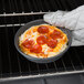 A person using a Chicago Metallic Deep Dish Pizza Pan to bake a pizza.