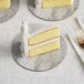 A slice of yellow cake with white frosting on an Enjay marble and wood laminated cake board with a fork.