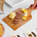A person holding an Enjay Marble/Wood Reversible Charcuterie Board with cheese and sausage.