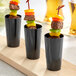 A group of black Choice plastic cups with meat and vegetables in them.
