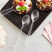 Two Visions clear plastic tasting spoons with dessert in small bowls.