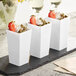 A group of white Choice square plastic mini cups with strawberries and nuts inside.