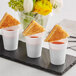 A group of white Choice plastic tiny shot glasses filled with soup on a tray.