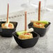Three black square plastic mini bowls filled with food on a table.