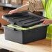 A woman in a safety vest opening a black plastic box with a Lavex utility lid.