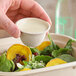 A person holding a World Centric compostable fiber portion cup of white liquid over a bowl of salad.