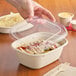 A person holding a World Centric clear plastic lid over a container of food.