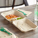 A World Centric compostable fiber clamshell container with food on a table with a green plastic fork.