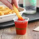 A hand holding a World Centric compostable plastic cup with ketchup and a french fry in it.