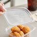 A hand holding a World Centric clear plastic container filled with fried chicken.