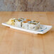A Blue Bamboo rectangular melamine plate with sushi on it sitting on a wood table.