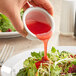 A hand pouring Kraft Fat-Free Raspberry Vinaigrette over a salad.