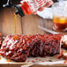 A hand pouring Mike's Hot Honey onto a piece of ribs.