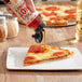 A hand pouring Mike's Hot Honey onto a slice of pizza.