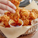 A hand dipping a piece of fried chicken into a Mike's Hot Honey dip cup.