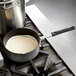 A Thunder Group anodized aluminum sauce pan with white liquid on a stove top.