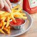 A hand dipping a french fry into a small bowl of Heinz Ketchup.