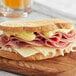 A sandwich with ham and cheese and Grey Poupon Dijon Mustard on a wooden board.