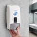 A hand pressing a button on a Safeguard Professional manual hand sanitizer dispenser on a wall.