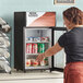 A woman with a tattoo on her arm opening the swing door on a black Avantco countertop refrigerator.
