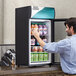A man taking a drink from a black Avantco countertop refrigerator.