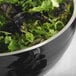 A Vollrath black metal serving bowl filled with green and black lettuce.