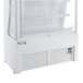 An Avantco white refrigerated air curtain merchandiser with shelves and a customizable panel.