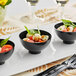 A group of small black bowls with food in them on a table.