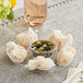 A Choice clear plastic mini circular dip tray filled with dumplings and sauce.