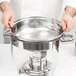 A person holding a Vollrath stainless steel water pan.