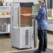 A woman standing in front of an Avantco stainless steel food dehydrator with glass doors.