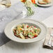 A warm gray Acopa Condesa porcelain pasta bowl filled with pasta, artichokes, and meat.
