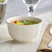 An Acopa Condesa warm gray porcelain bouillon cup filled with soup and vegetables on a table.