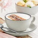 A gray matte stoneware cup with a matching saucer, filled with a frothy beverage and garnished with chocolate shavings and cinnamon.